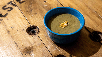 a blue bowl of green soup on a wooden table made from a cable spool